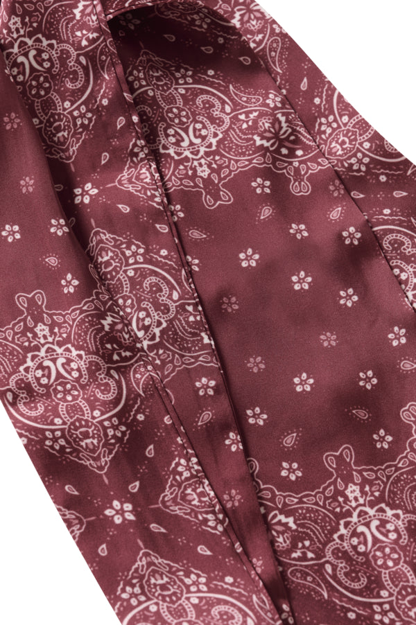 A close-up of a burgundy satin necktie with a white paisley and floral bandana pattern, shown against a plain white background.