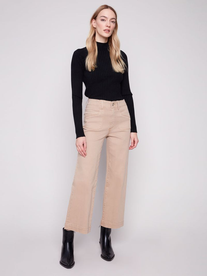 Woman wearing a black ribbed sweater and beige high-waisted pants on a white background