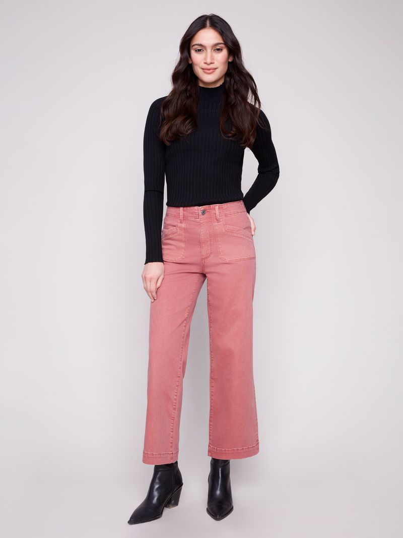 Woman wearing a black sweater and pink pants against a white background