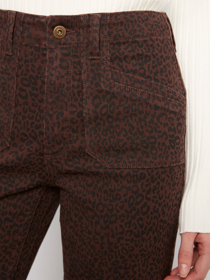 Close-up of dark brown leopard-print jeans worn by a model, showing the back pocket, button, and part of the white ribbed top and hand.