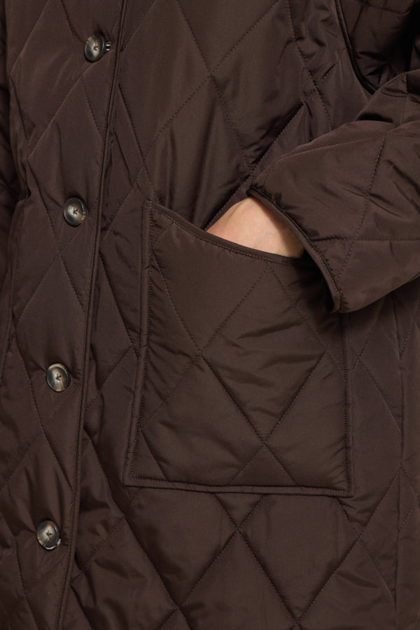Close-up of a dark brown quilted jacket with diamond stitching, a button closure, and a side pocket showing a hand inside.