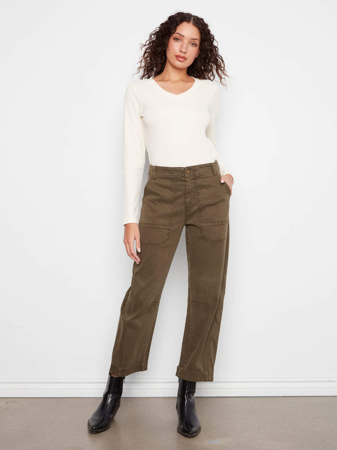 Woman wearing a white long-sleeve top and green pants against a white background