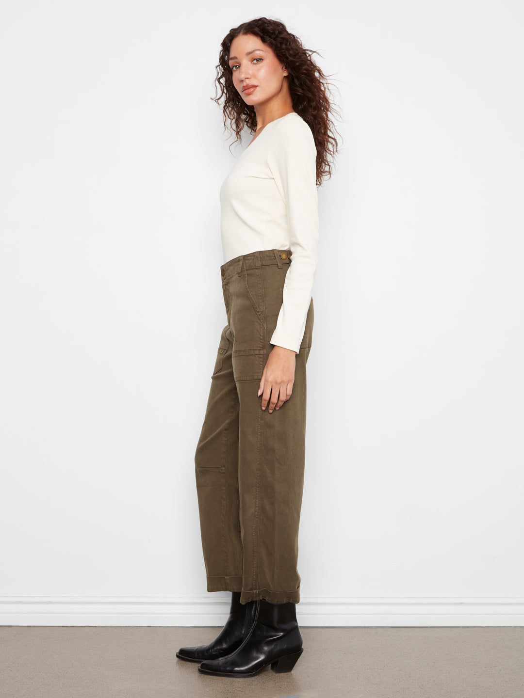 Woman wearing a white top and olive green pants against a plain background
