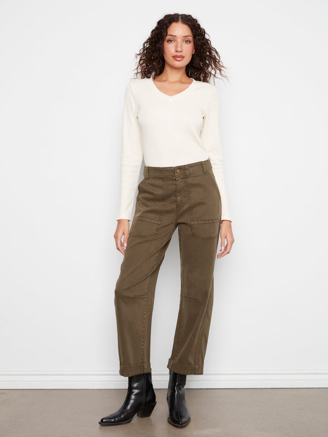 Woman wearing a white top and olive green pants against a white background