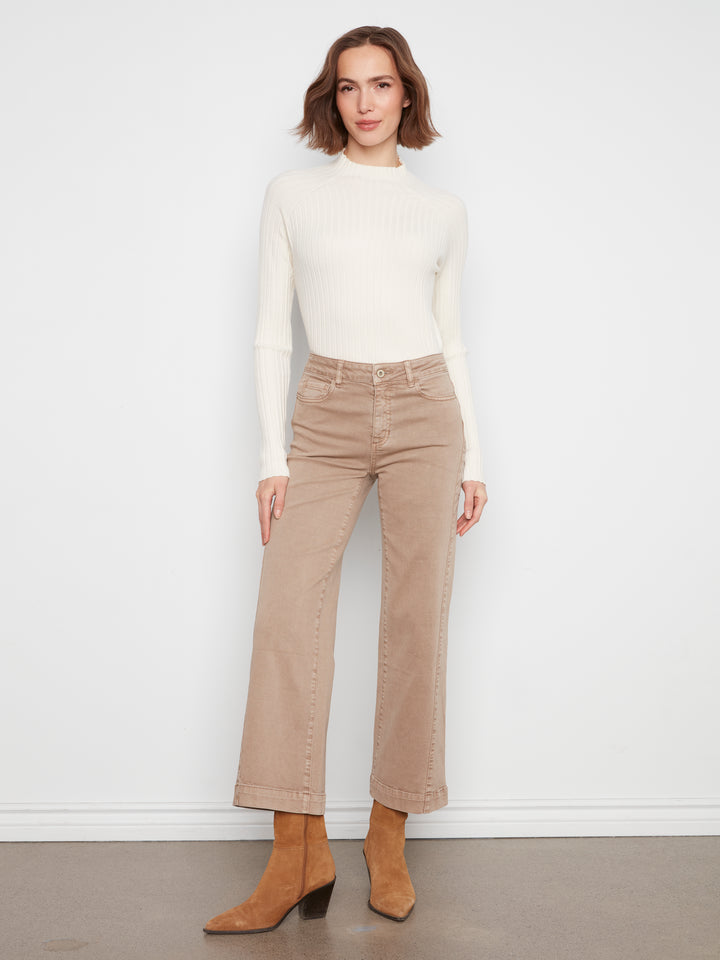 A woman modeling a cream ribbed mock-neck long-sleeve top and beige wide-leg cropped jeans with tan ankle boots, standing against a white wall.