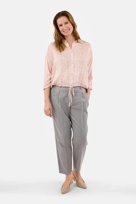 Woman wearing a light pink blouse and gray pants on a white background
