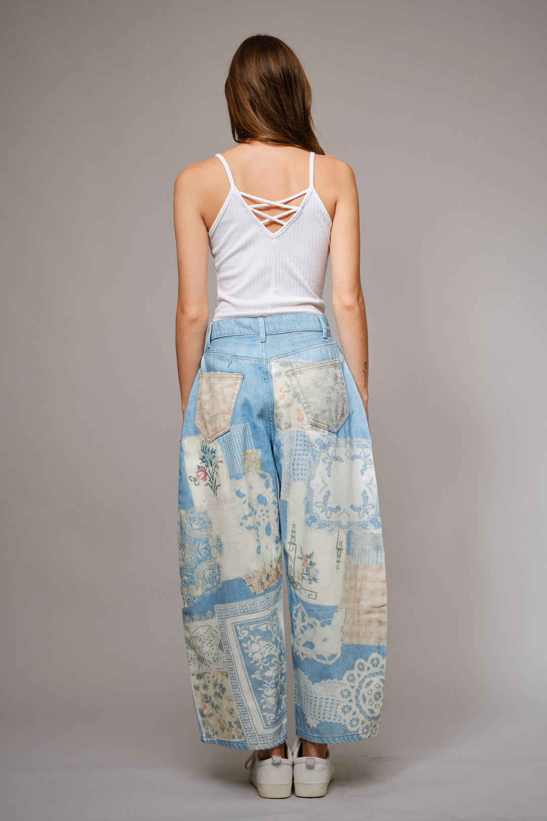 Woman wearing a white tank top and patterned blue pants on a gray background