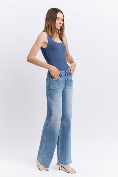 Woman wearing a blue bodysuit and light blue jeans on a white background