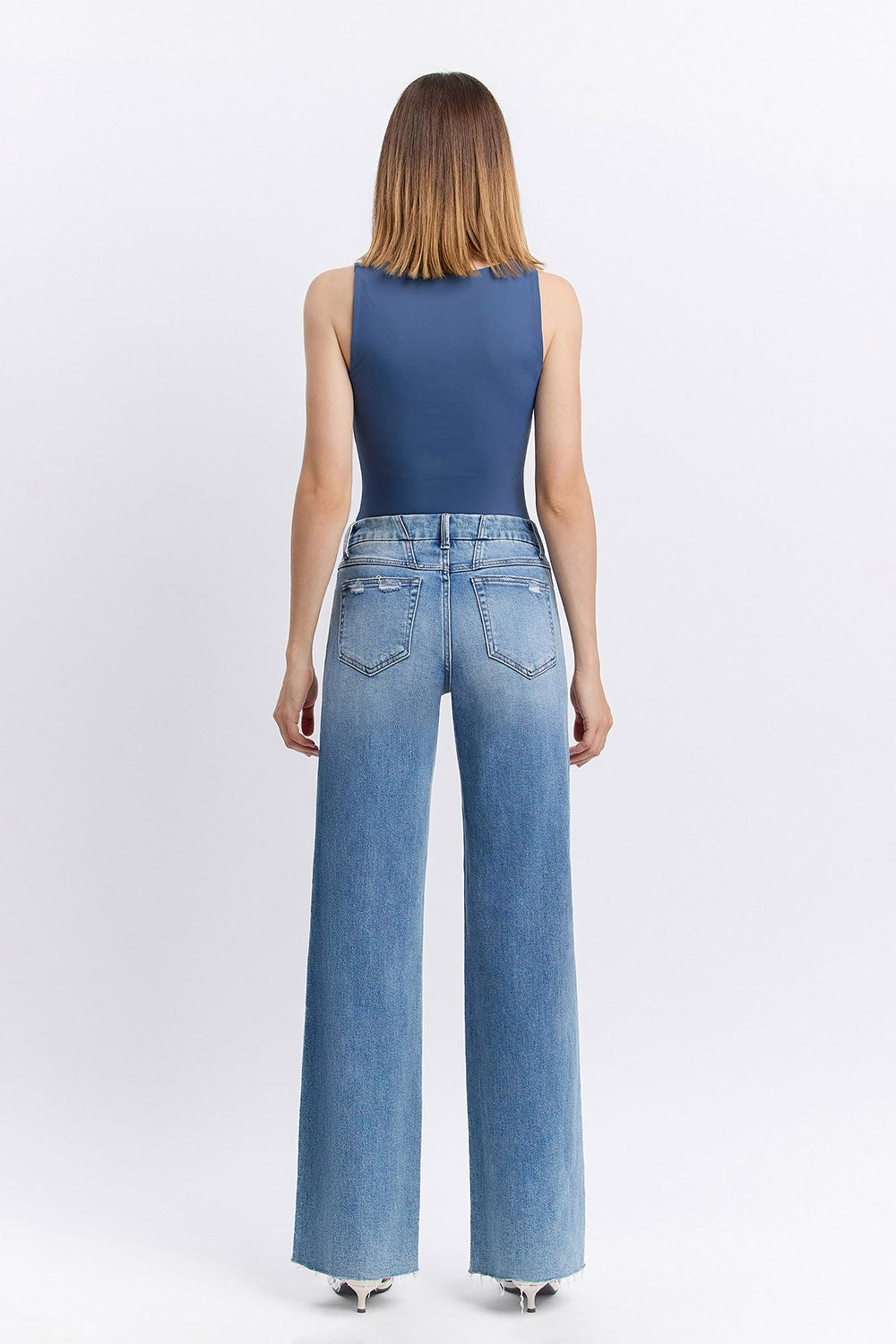 Woman wearing a blue sleeveless top and light blue jeans on a white background