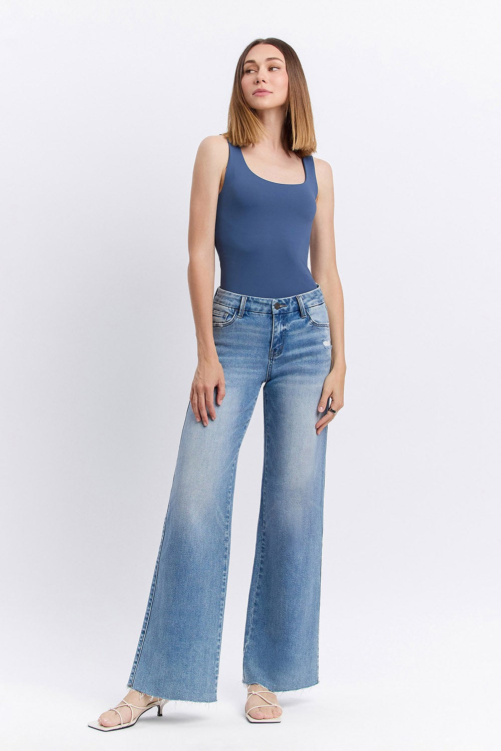 Woman wearing a blue tank top and light blue jeans on a white background