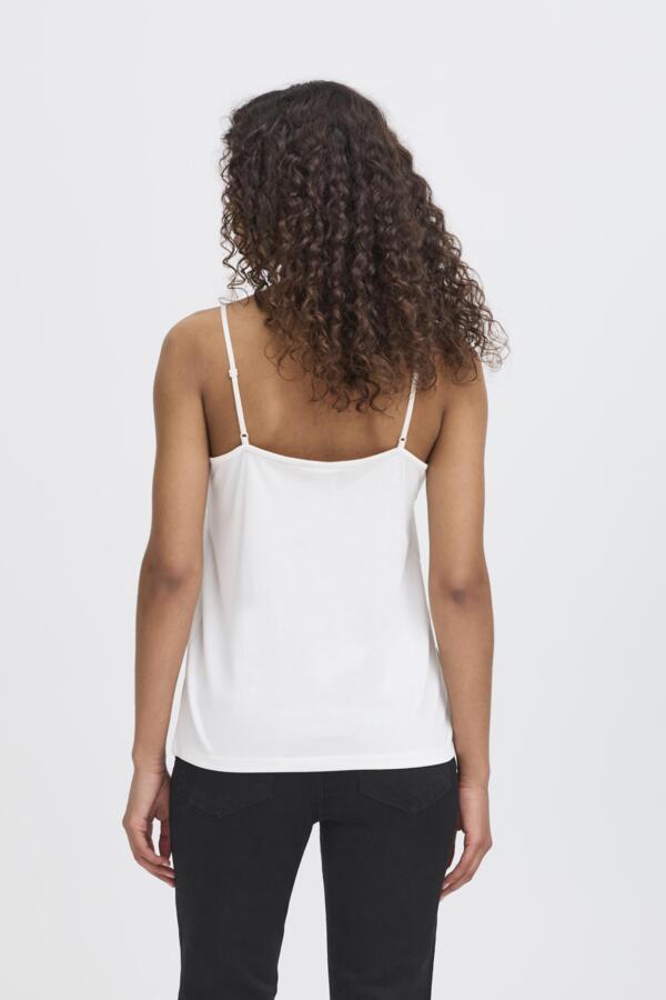 Person wearing a white spaghetti strap top and black pants on a plain background