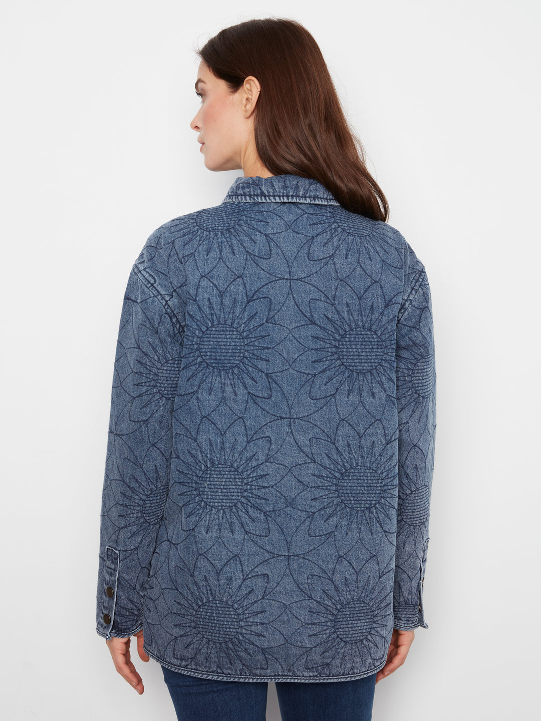 A woman shown from the back wearing a blue denim jacket with a large sunflower embroidery pattern, set against a plain white background.