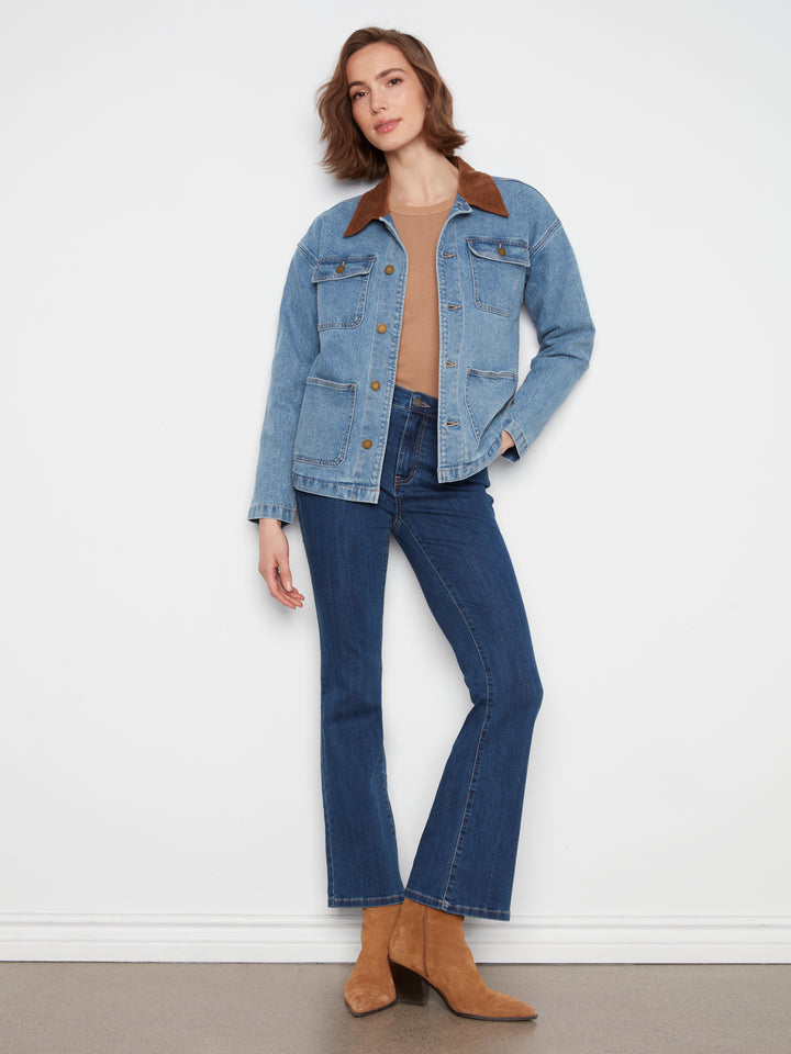 A woman modeling a light blue denim jacket with a brown corduroy collar, paired with dark blue jeans and tan suede ankle boots, standing against a white wall.
