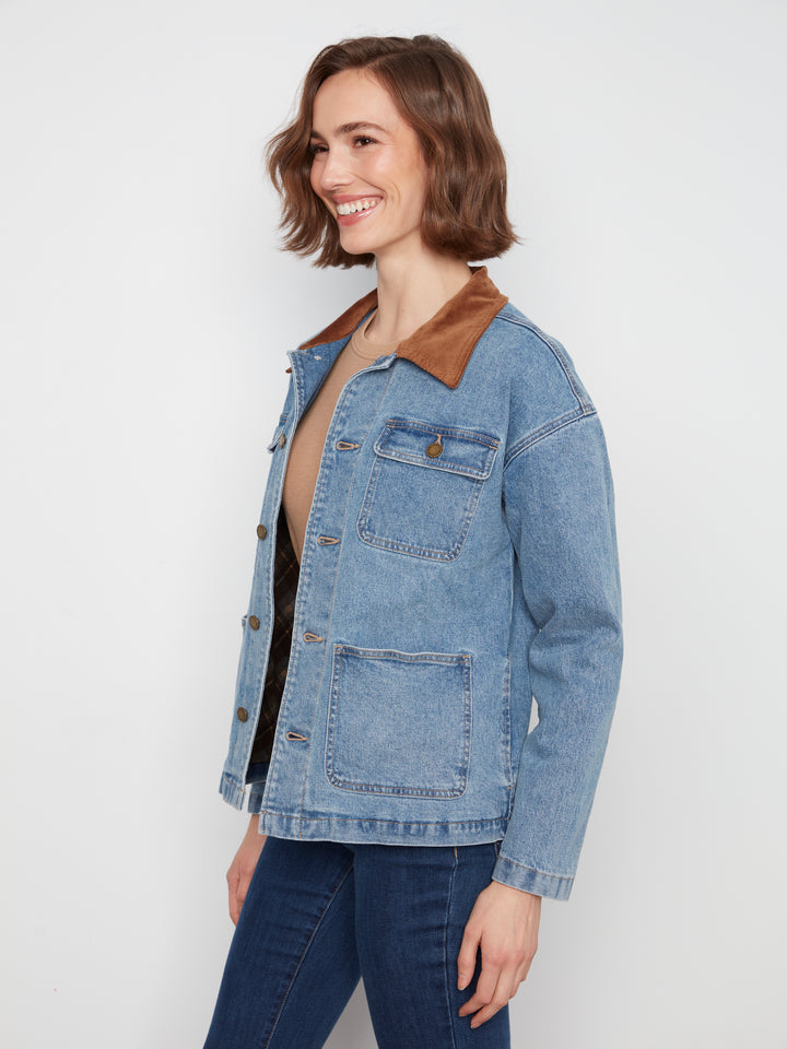 A woman wearing a light blue denim jacket with a brown corduroy collar, paired with a black top and dark blue jeans, photographed against a plain white studio background.