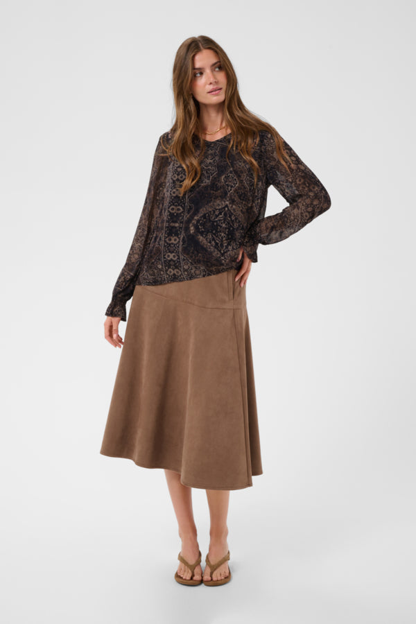 A woman modeling a long-sleeve black lace top paired with a brown A-line midi skirt and flat sandals, photographed against a light gray studio background.