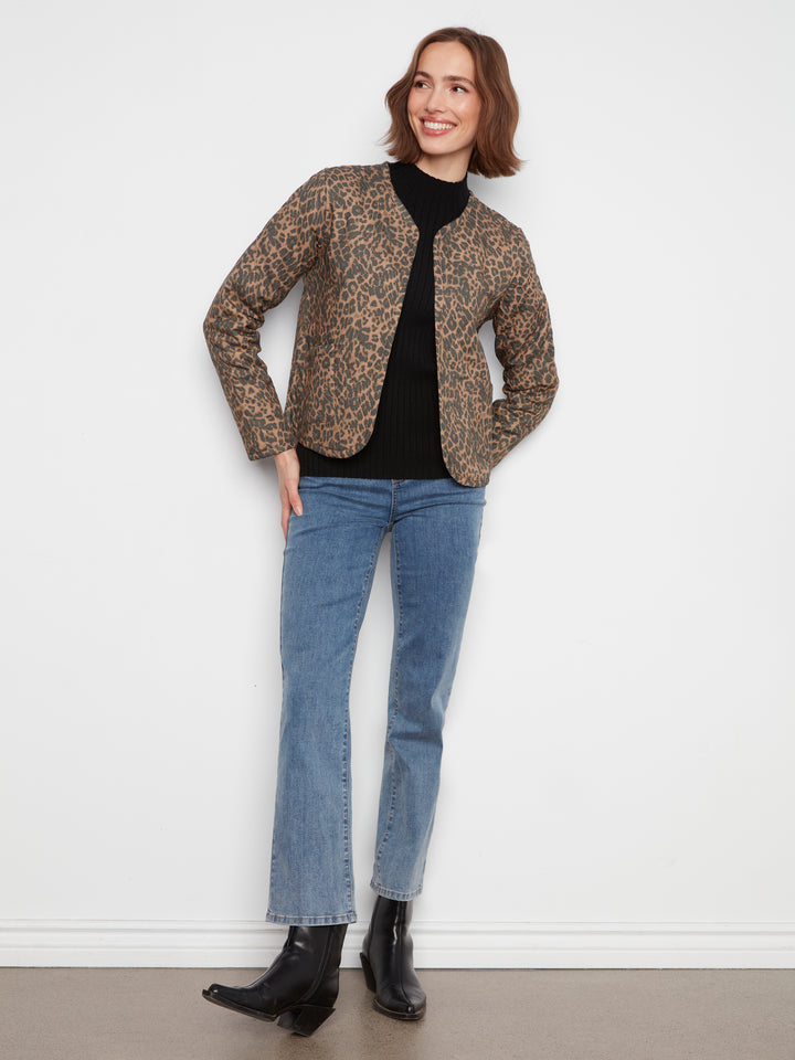 A woman modeling a cropped leopard-print jacket over a black turtleneck, paired with blue jeans and black ankle boots, standing against a plain white wall.