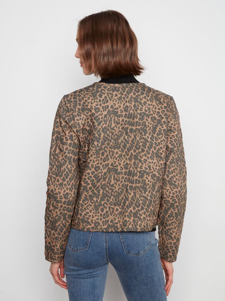 A woman viewed from the back wearing a cropped leopard-print jacket with a black collar and blue jeans, against a plain light gray studio background.