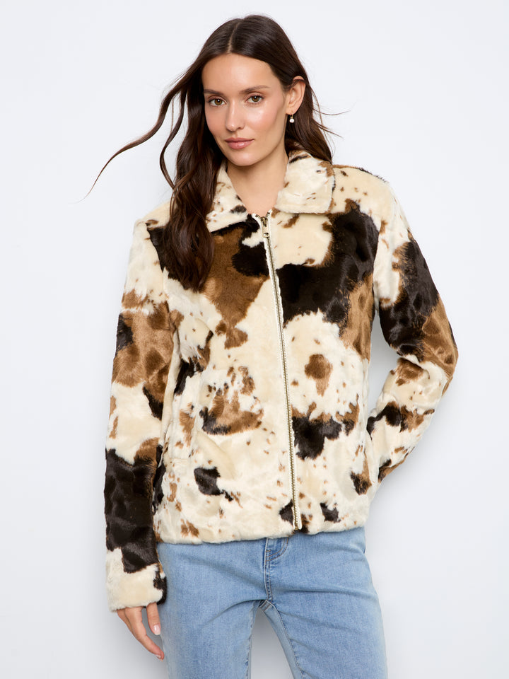 A woman wearing a faux fur zip-up jacket with a brown, black, and beige cow print pattern, paired with light blue jeans, against a plain white background.
