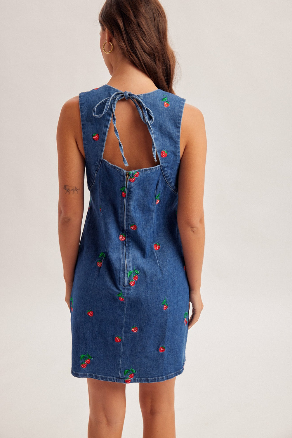 Blue denim dress with cherry embroidery on a plain background