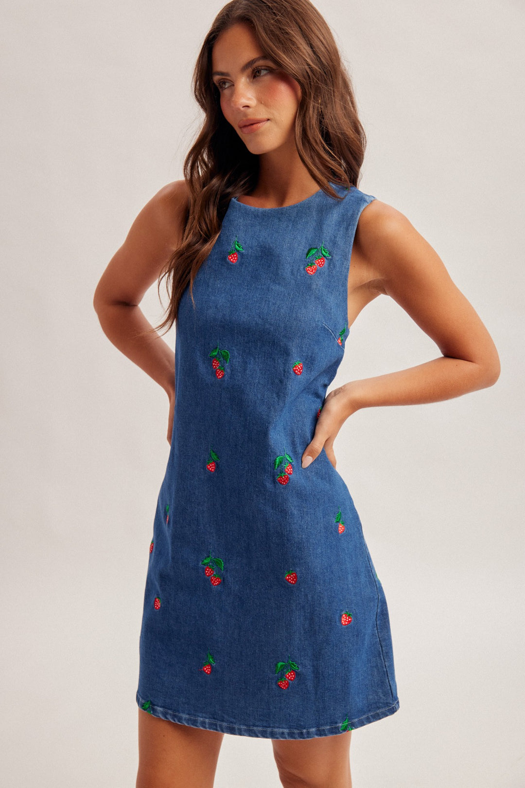 Woman wearing a blue dress with cherry patterns on a plain background