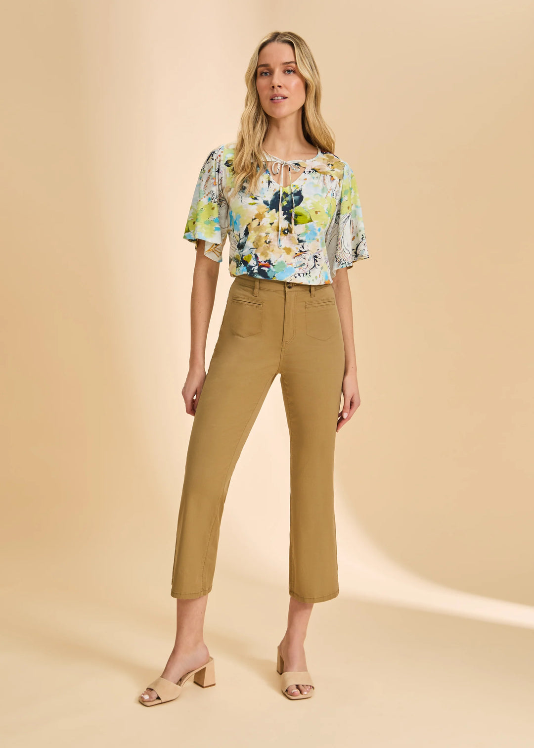 Woman wearing a floral blouse and beige pants on a beige background