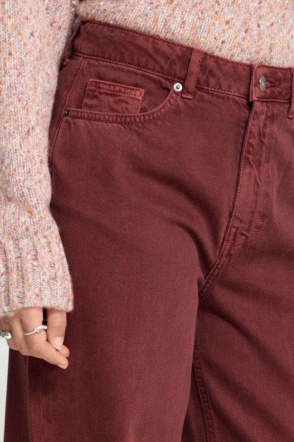 Close-up of a person wearing rust-brown or burgundy denim jeans with a speckled cream knit sweater visible at the top and left side.