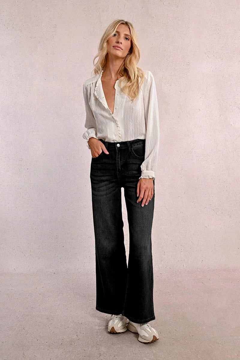 Woman wearing a white blouse and black jeans against a plain background