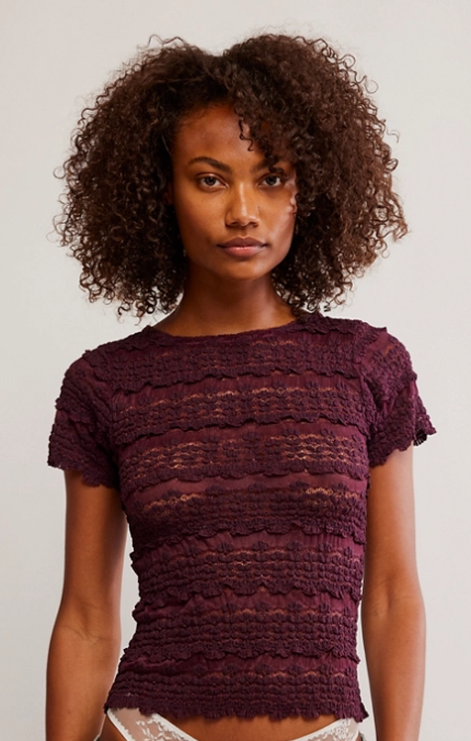 Woman wearing a maroon textured top and blue jeans against a plain background