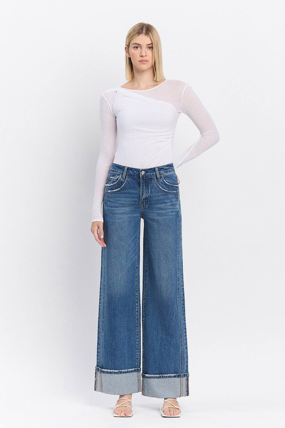 Woman wearing a white long-sleeve top and blue jeans on a white background