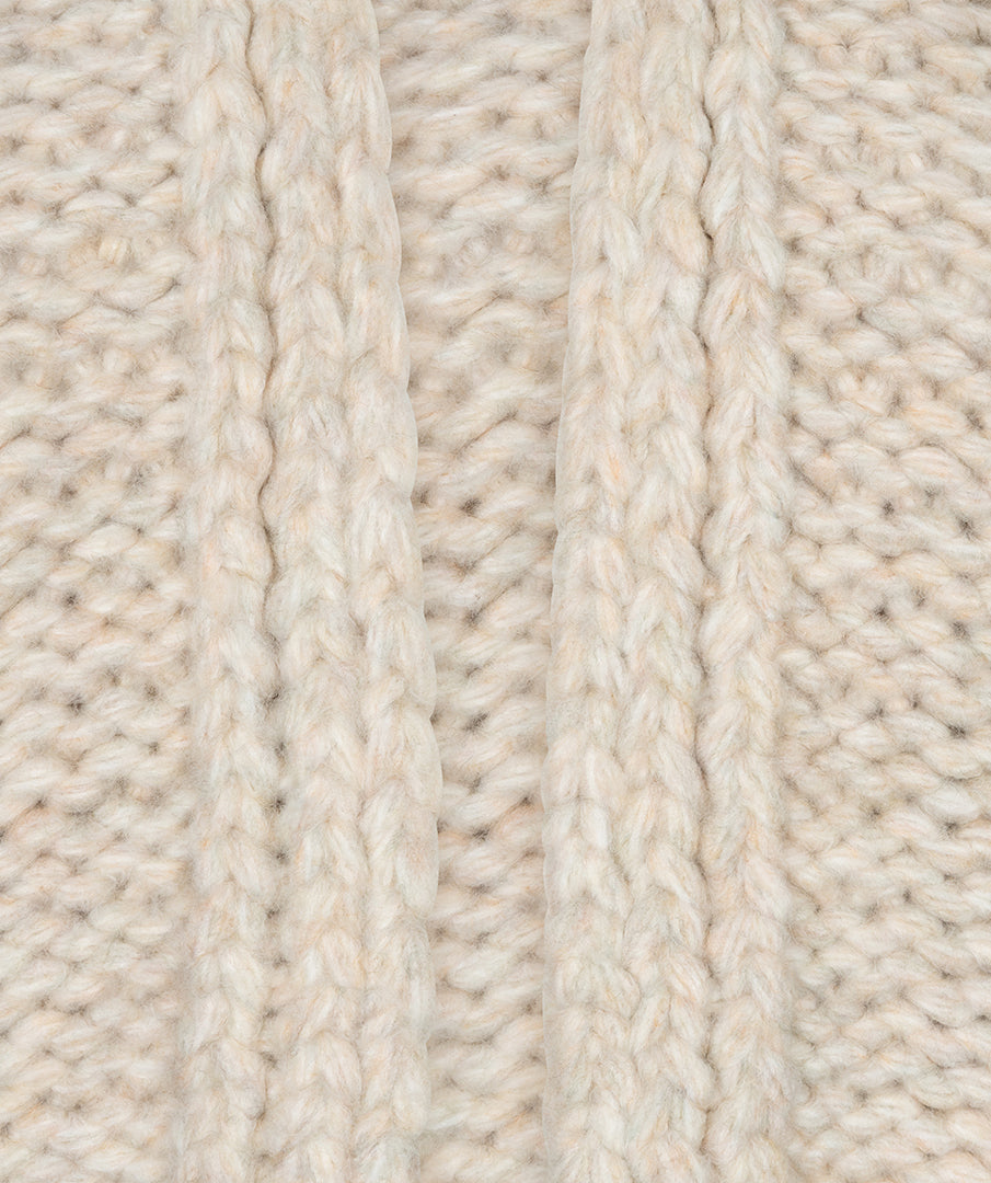 Close-up of a cream-colored chunky knit fabric with vertical ribbed and cable stitch patterns.