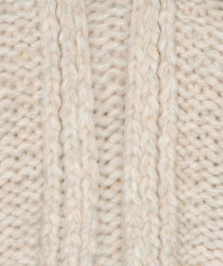 Close-up of a cream-colored chunky knit fabric with vertical ribbed and cable stitch patterns.
