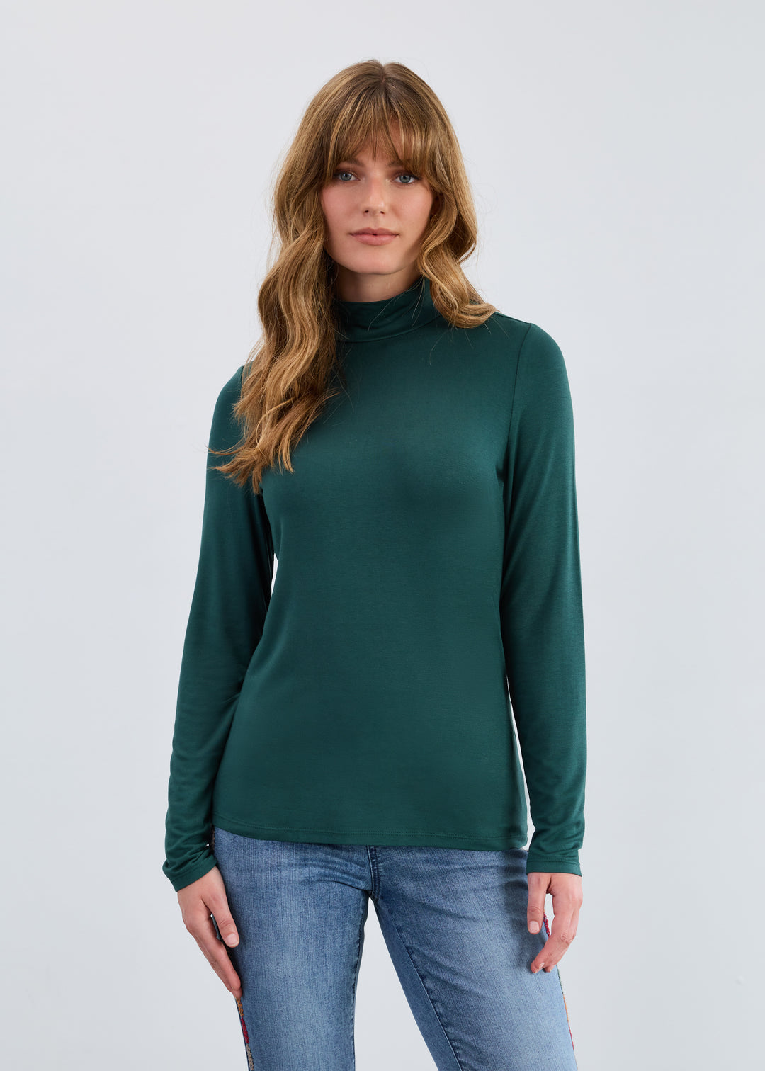 Woman wearing a green turtleneck sweater and blue jeans on a light gray background