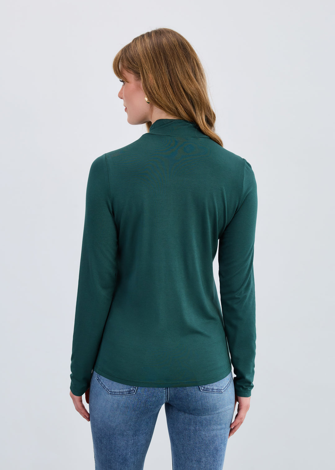 Woman wearing a green long-sleeve top and blue jeans on a light gray background