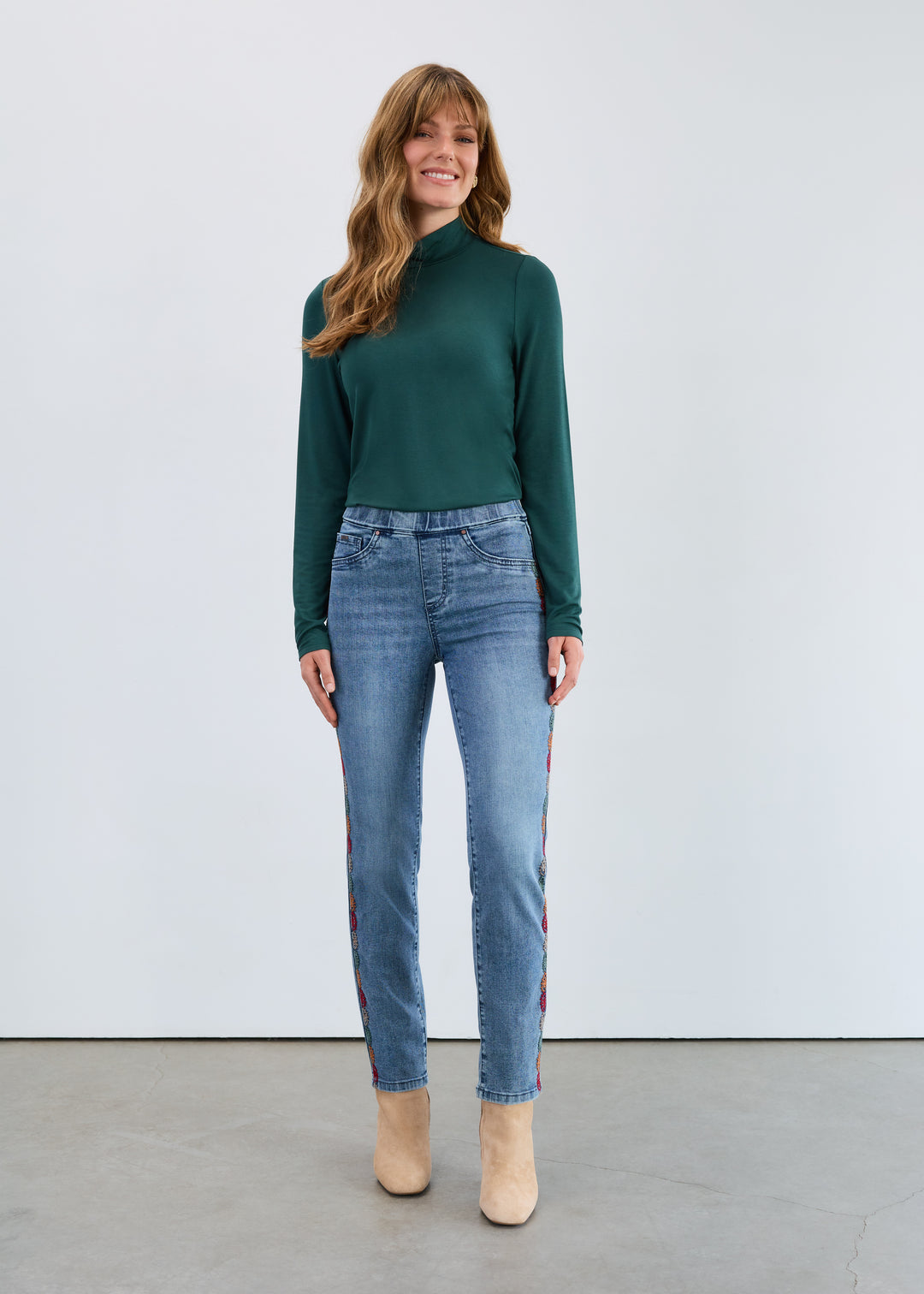 Woman wearing a green sweater and blue jeans standing against a white background