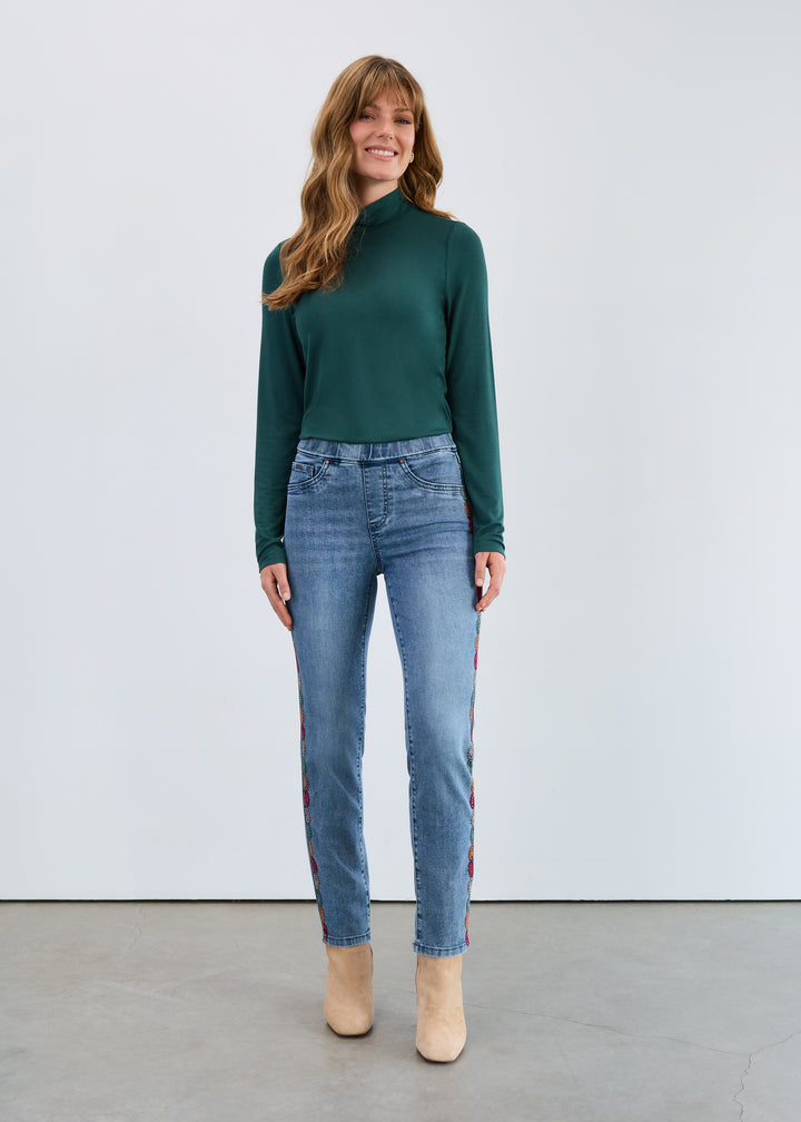 Woman wearing a green sweater and blue jeans standing against a white background