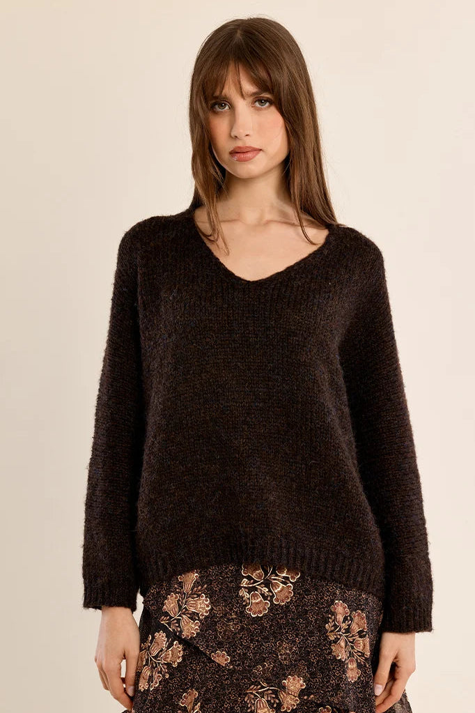 A woman modeling a dark brown fuzzy knit V-neck sweater paired with a brown floral patterned skirt, set against a plain beige studio background.