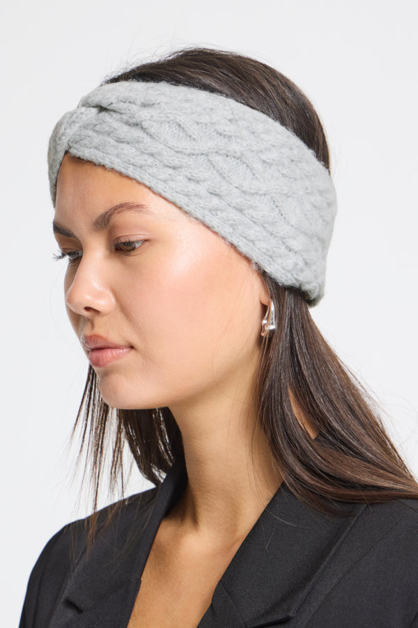 A woman wearing a light gray cable-knit twisted headband, shown in profile against a plain light gray background.
