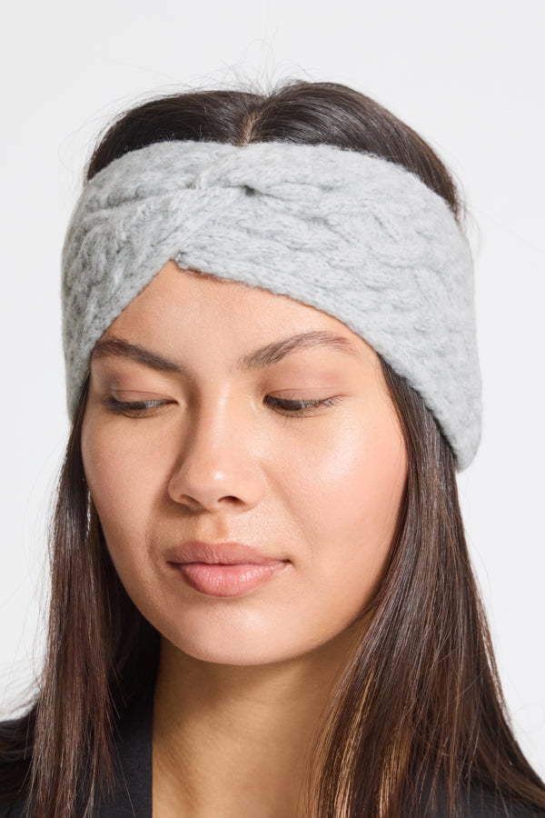 A woman wearing a light gray cable-knit twisted headband, shown in a close-up portrait against a plain light background.