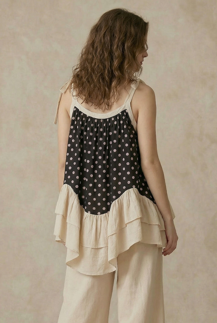 Woman wearing a layered outfit with a polka dot top and beige pants against a neutral background