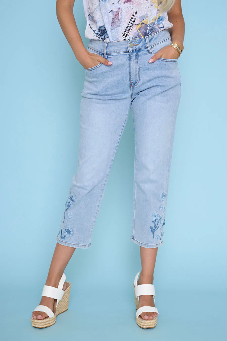 Person wearing light blue jeans with floral patterns against a solid background