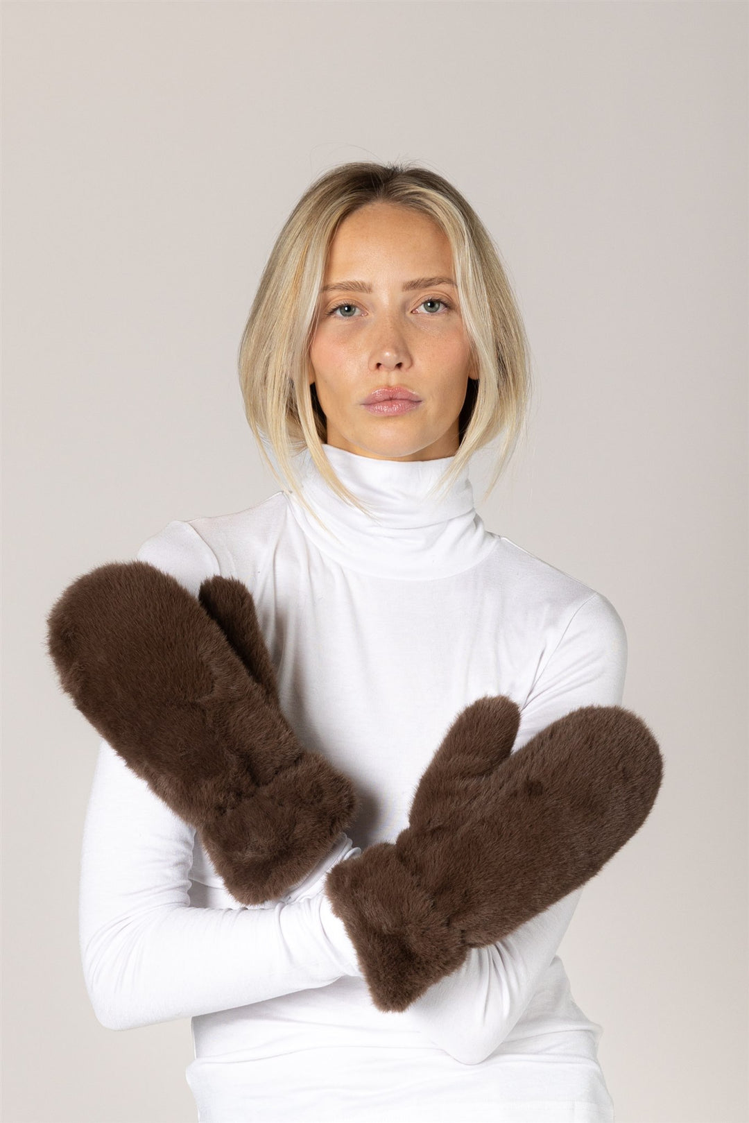 Person wearing brown mittens with a plain background