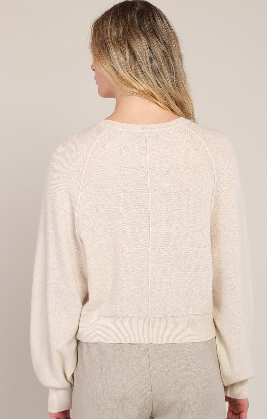 Person wearing a beige sweater and pants against a neutral background