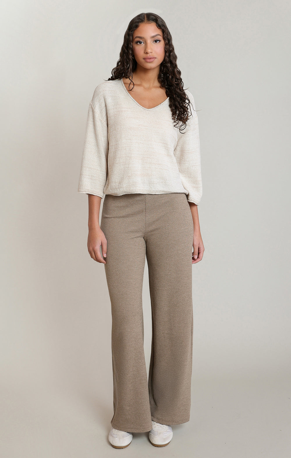 Woman wearing a white sweater and beige pants on a plain background
