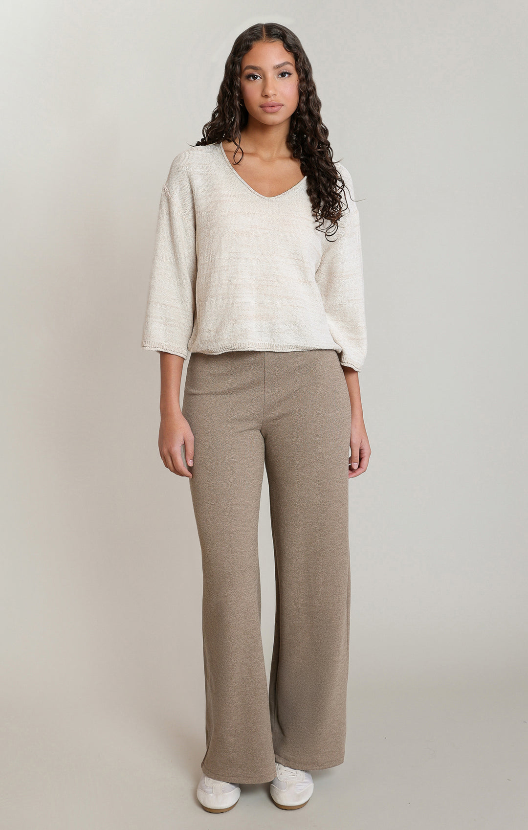 Woman wearing a white sweater and beige pants on a plain background