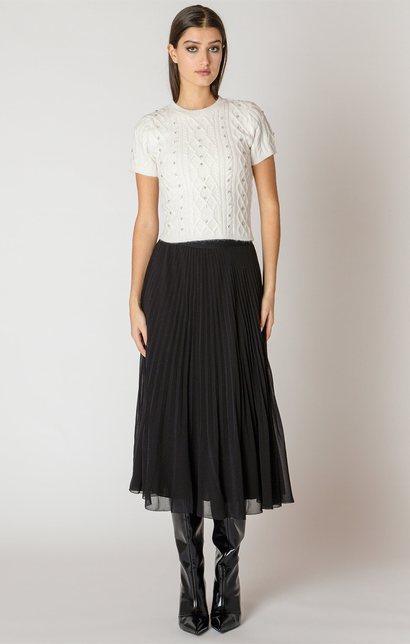 Woman wearing a white lace top and black pleated skirt on a plain background