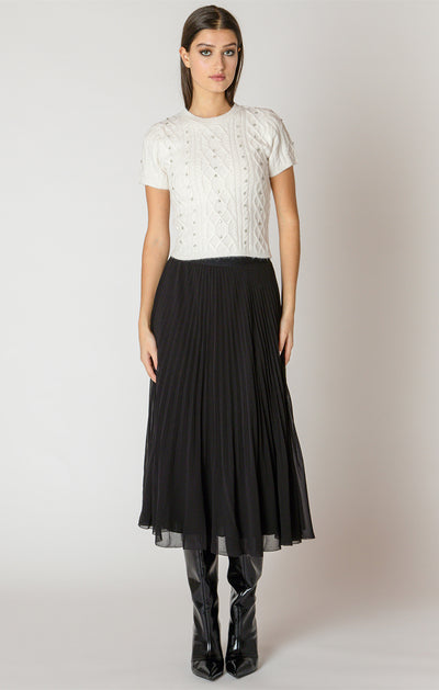 Woman wearing a white lace top and black pleated skirt on a plain background