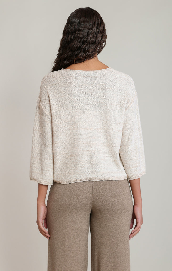 Woman wearing a light beige sweater and brown pants against a neutral background