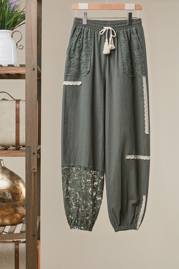 Green pants with lace details hanging on a wooden rack.