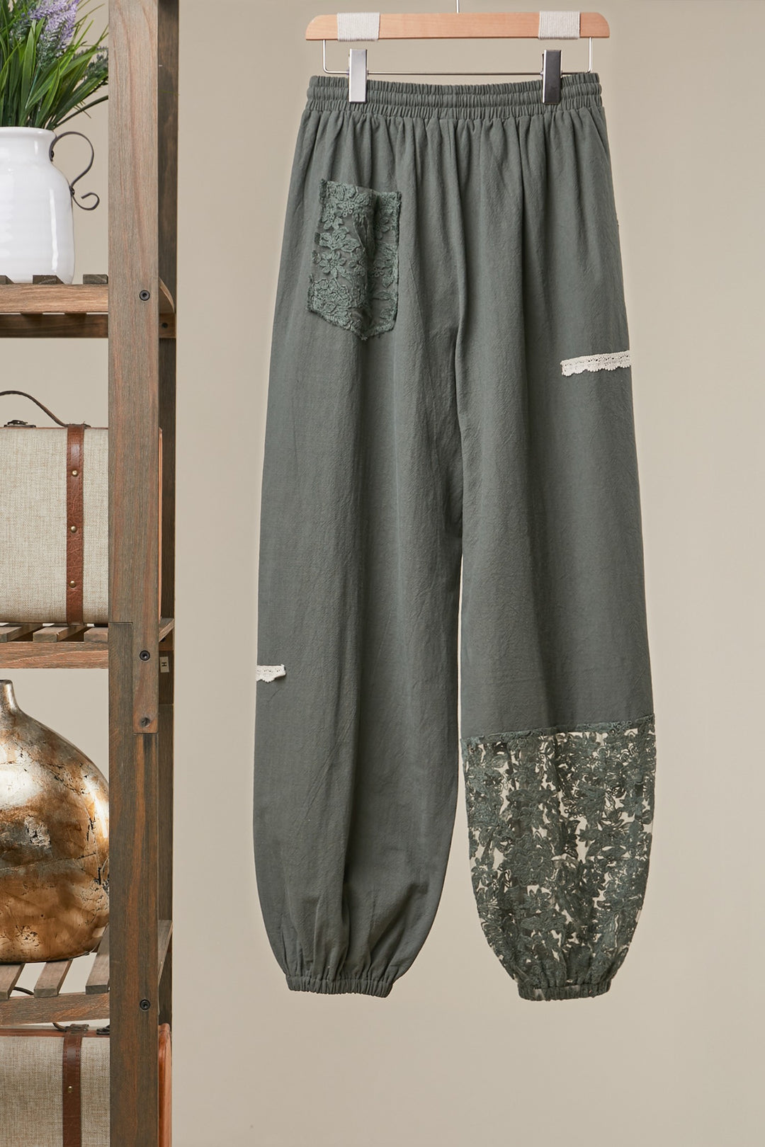 Green pants with floral patch on a hanger against a beige wall.