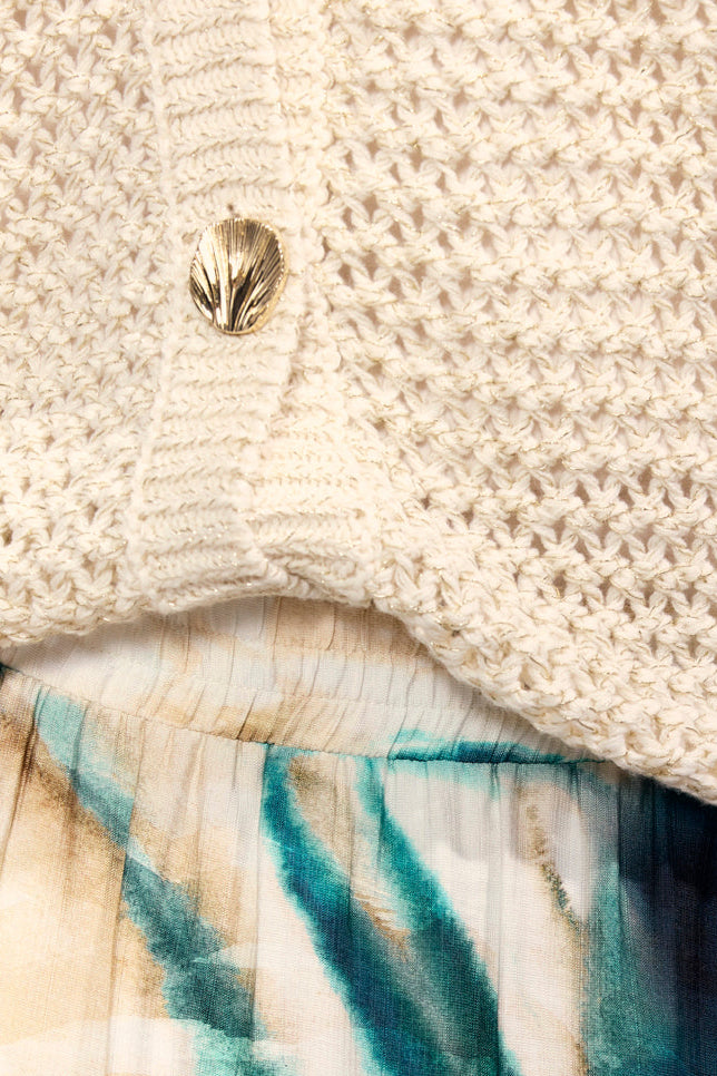 Close-up of a person wearing a textured beige sweater and tie-dye pants with gold jewelry.